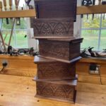 A picture of a stack of wooden walnut boxes that have been carved with a 17th century style relief carving design. Carved by Shea Alexander with the Alexander Brothers