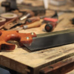 Picture of a Dennis Wayne backsaw with a cherry handle sitting on a woodworking bench with other tools