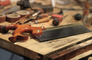 Picture of a Dennis Wayne backsaw with a cherry handle sitting on a woodworking bench with other tools