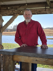 Wayne Fry Plane Wellness Teacher Standing with a Table he made with wood and concrete