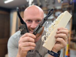 James Wright holding two spoke shaves and a piece of wood with spoke shave shavings on it